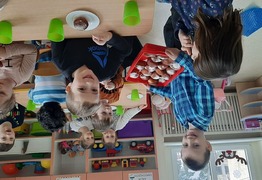 Dzieci z grupy Żabusie (ul. Nowa) podczas świętowania dnia Tłusty Czwartek. Chłopiec częstuje pozostałe dzieci pączkami (photo)