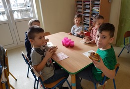Dzieci z grupy Pingusie (ul. Nowa) podczas świętowania dnia Tłusty Czwartek. Dzieci siedzą przy stolikach i jedzą pączki (photo)