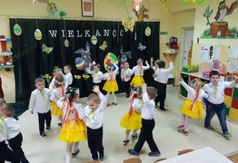 Dzieci z grupy Kubusie Puchatki (Gołębin Stary) podczas tańca.  Chłopcy ubrani na galowo, dziewczynki w żółte spódniczki i białe bluzki, na głowach maja opaski w kwiatki (photo)